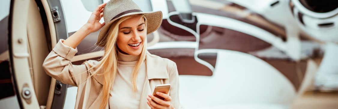 Young successful girl getting out of a private jet parked on a runway. She is using a mobile phone.